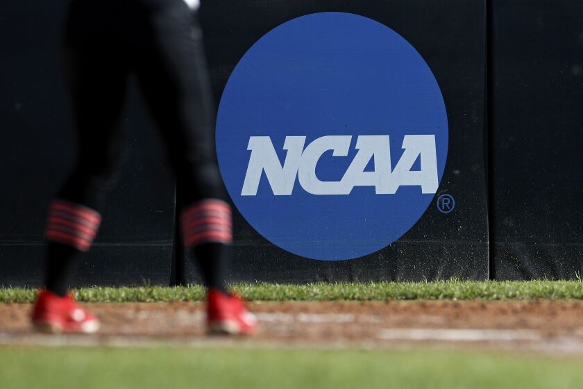 FILE - In this April 19, 2019, file photo, an athlete stands near a NCAA logo during a softball game in Beaumont, Texas. The NCAA is poised to take a significant step toward allowing college athletes to earn money without violating amateurism rules. The Board of Governors will be briefed Tuesday, Oct. 29 by administrators who have been examining whether it would be feasible to allow college athletes to profit of their names, images and likenesses. A California law set to take effect in 2023 would make it illegal for NCAA schools in the state to prevent athletes from signing personal endorsement deals. (AP Photo/Aaron M. Sprecher, File)