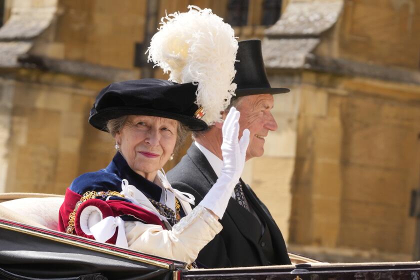 Princess Anne waving at the crowd wearing a feathered hat and white gloves. 