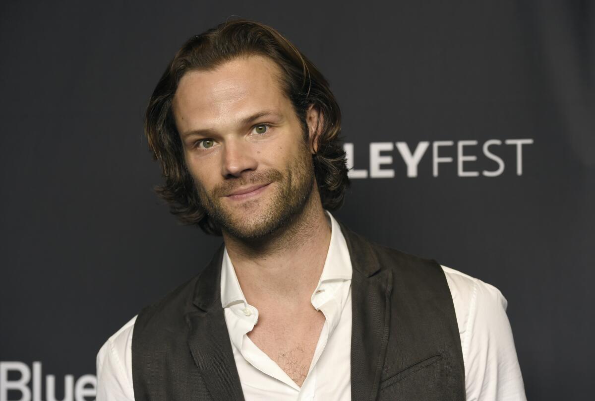 Jared Padalecki looking straight ahead in a white open-collar shirt under a gray vest