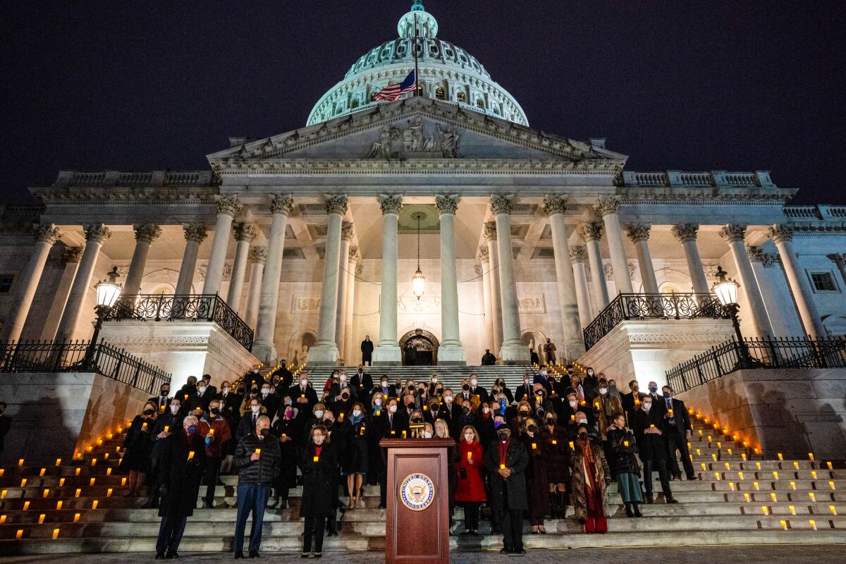 People stand holding candles on steps outside the Capitol in the dark.