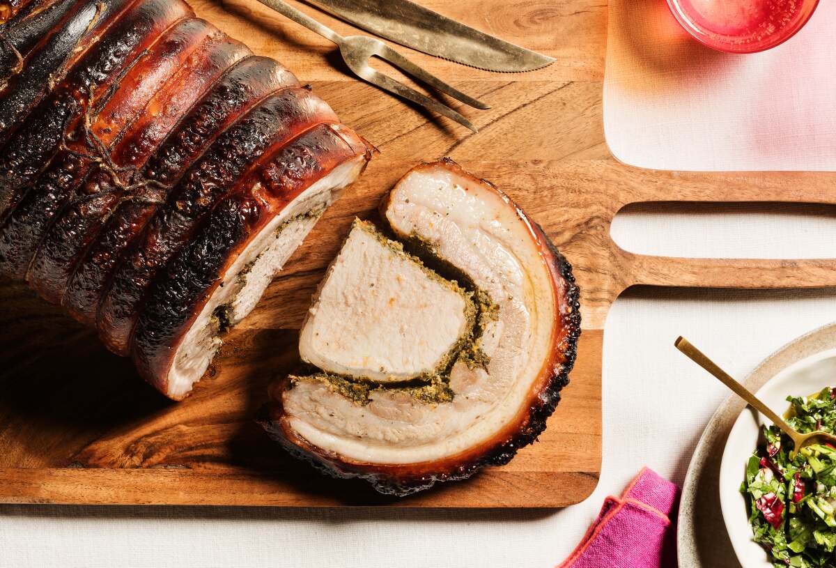 A whole porchetta with a slice lying next to it, and a bowl of green sauce