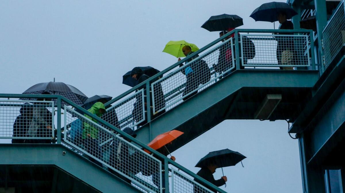 Early morning commuters at the Irvine Transportation Center walk down the stairway from an elevated pedestrian bridge, bundled with jackets and shielded from the rain, on Nov. 21, 2016.