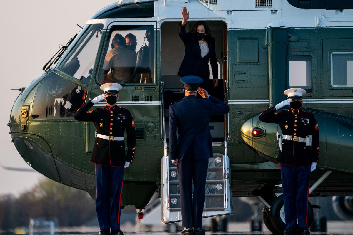 Vice President Kamala Harris waves from a helicopter with Marines standing at salute