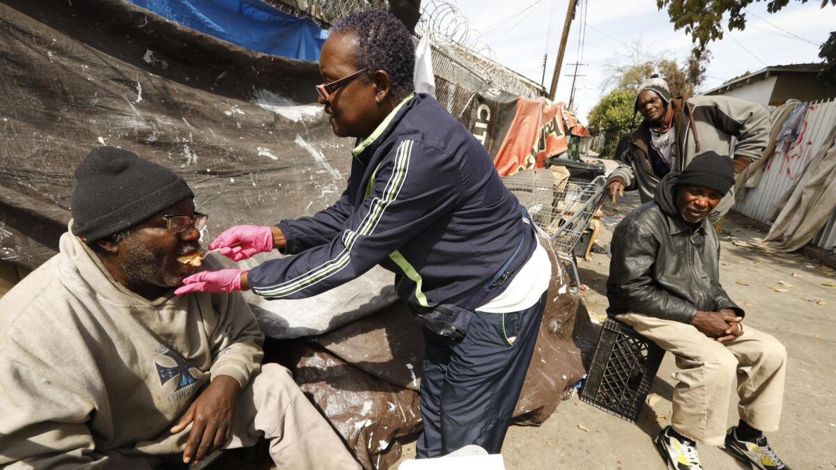 Rose Rios, 70, of Cover the Homeless Ministry, center, gives pie to Donald Shields, 59, who is legally blind and living in an alley in South Los Angeles.