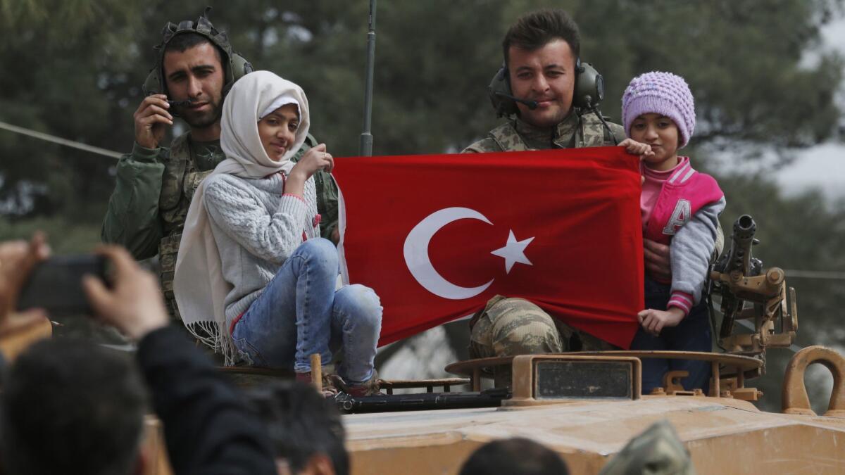 Turkish soldiers atop a tank pose for pictures with Syrian children holding a Turkish flag during a Turkish government-organized media tour on March 24, 2018, in the northwestern Syrian city of Afrin.