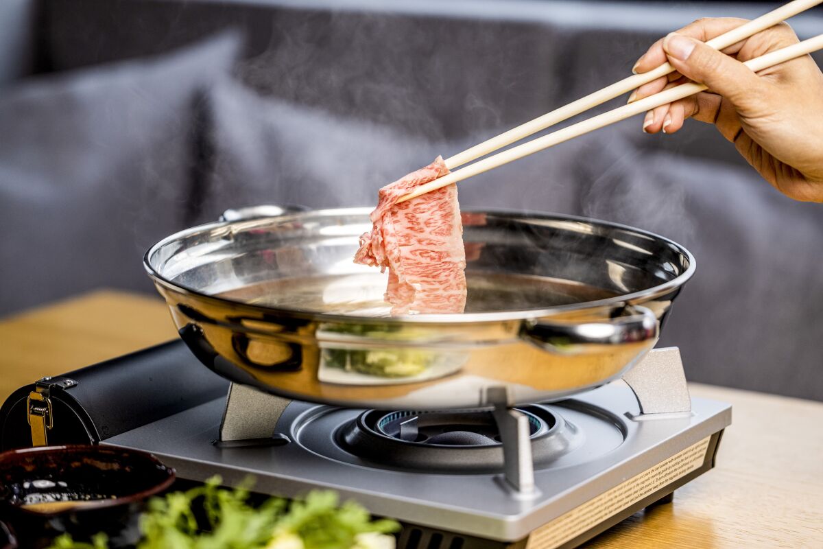 A photo of a hand holding chopsticks that grip a piece of heavily marbled Wagyu beef.