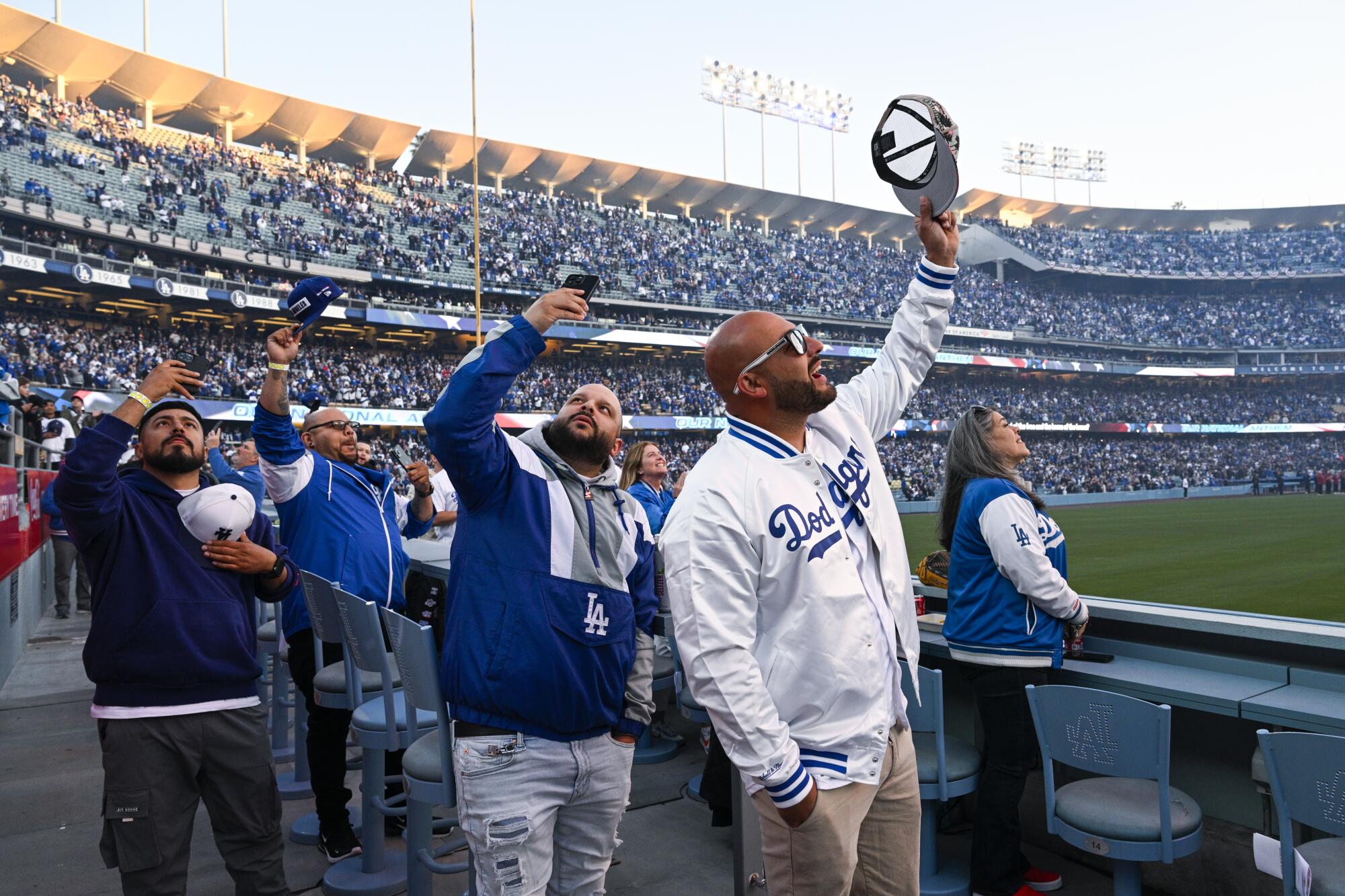 Fans remove their hats as they watch a military flyover above Dodger Stadium before the Dodgers' season opener.