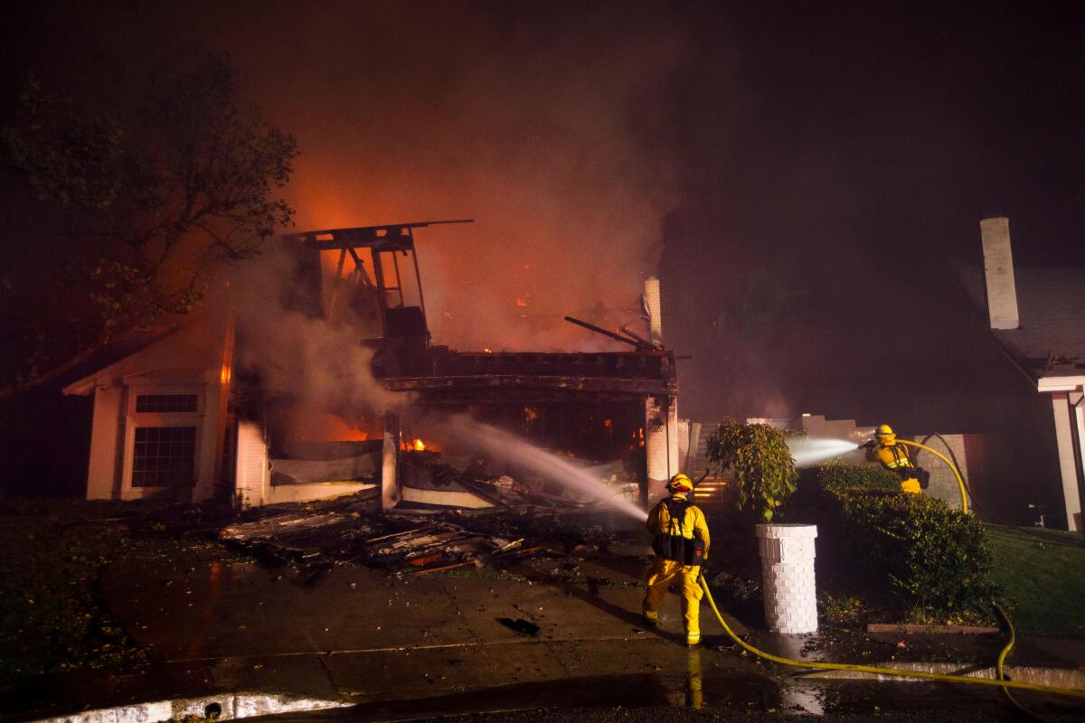 Two firefighters spray water on a house fire.