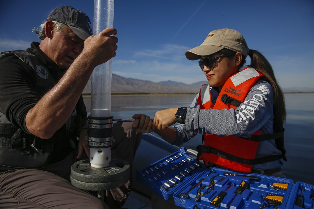 A man and woman on a raft prepare a corer to collect sediment.