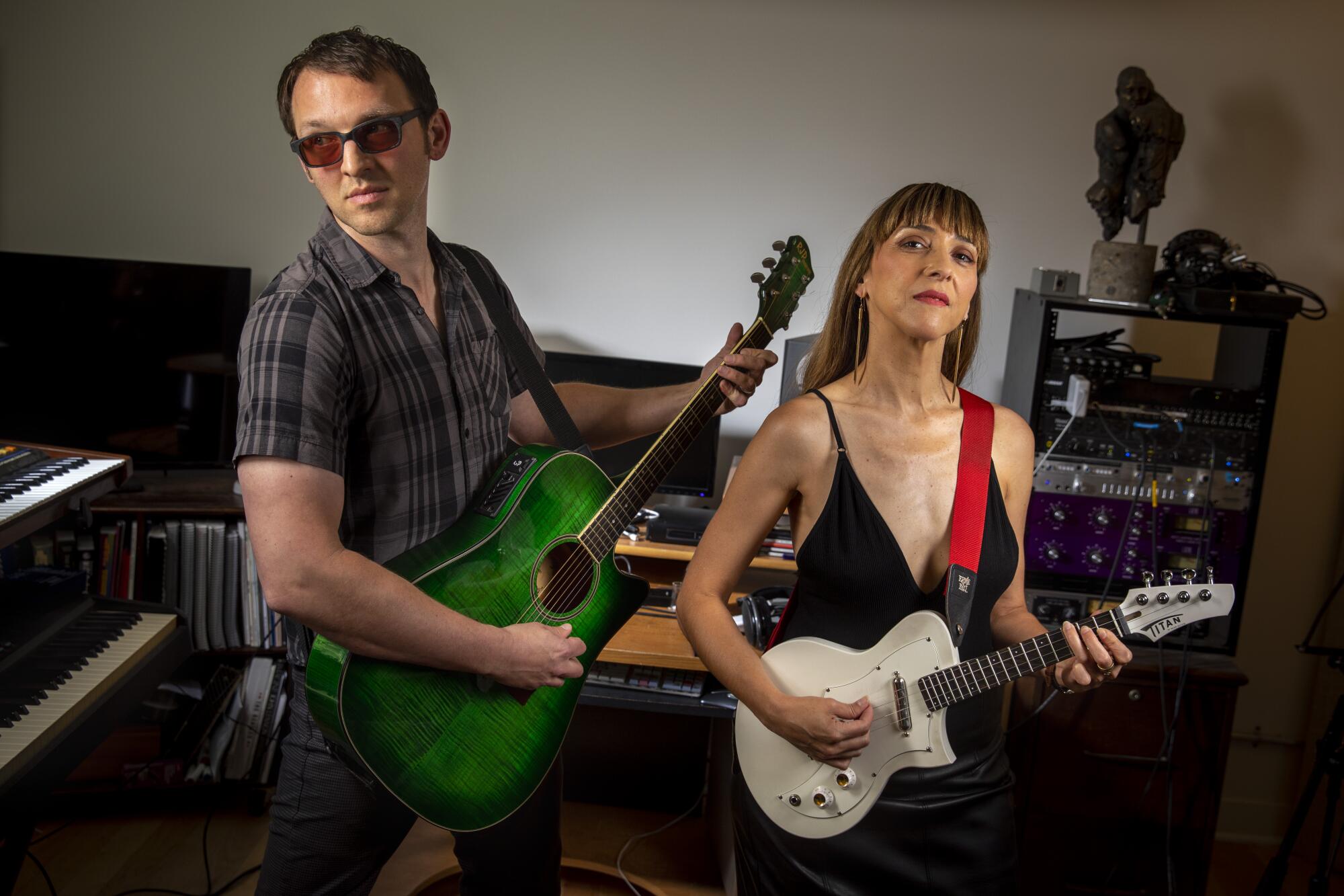 A man holding a green guitar and a woman strumming a white guitar