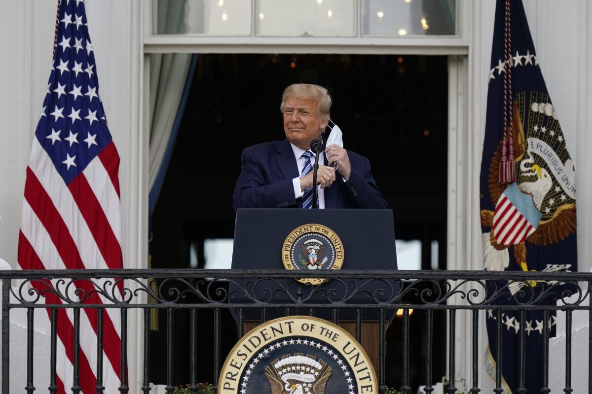 President Trump removes his face mask to speak from a balcony of the White House.