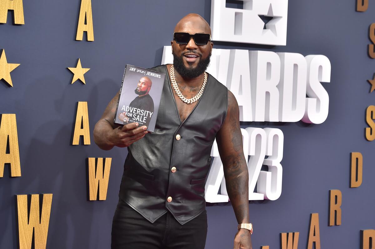 Jeezy smiles and poses with his memoir, "Adversity for Sale," while wearing sunglasses and a black vest
