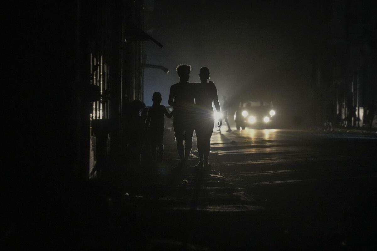 People walk on a dark city street lit by headlights.