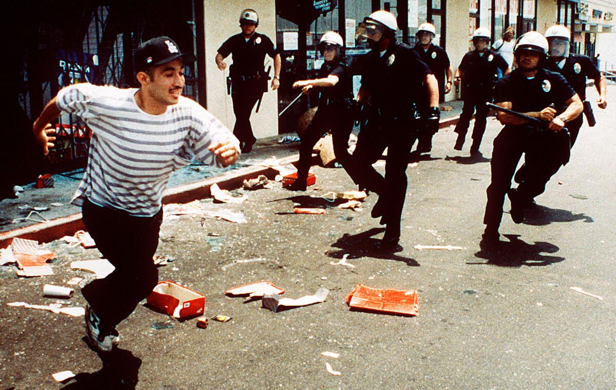 A man flees from a looted sporting goods store at Vermont and 1st Street as LAPD officers arrive on April 30, 1992.