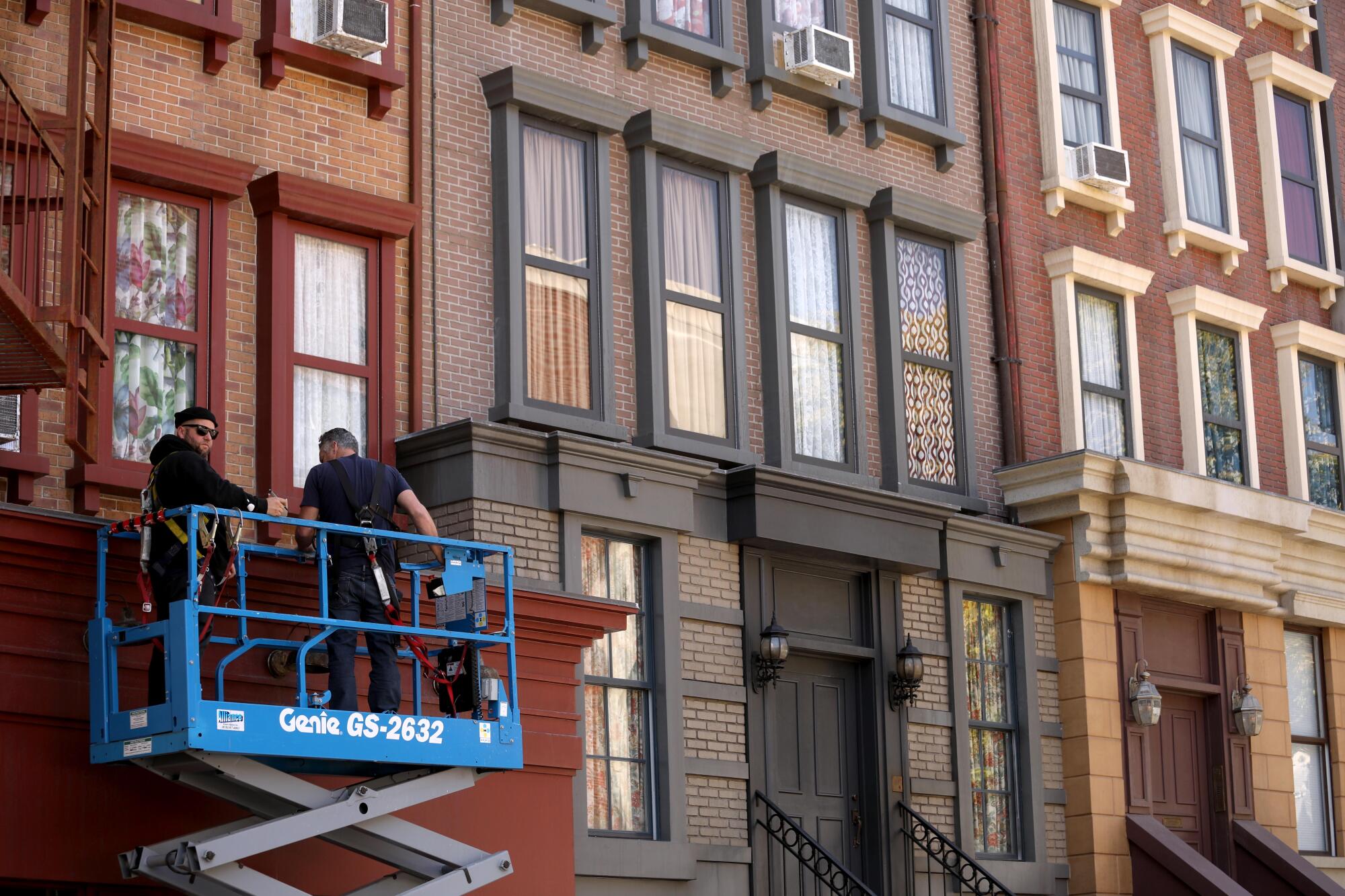 福克斯纽约片场，两名男子在剪刀式升降机上在一栋褐砂石建筑的外墙上工作。