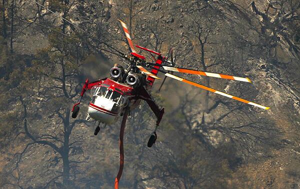 An air crane helicopter flies past a burned grove of trees after making a water drop in O'Neil Canyon in the hills above Lebec in Kern County, where firefighters managed to cut containment lines around a larger portion of the 1,300-acre wildfire.
