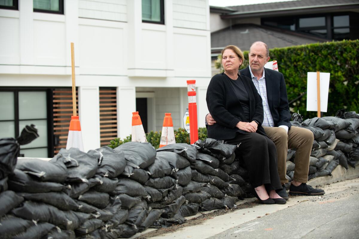Amy and Marshall Senk sit on sandbags lining the curb around their newly rebuilt home Friday, May 17.