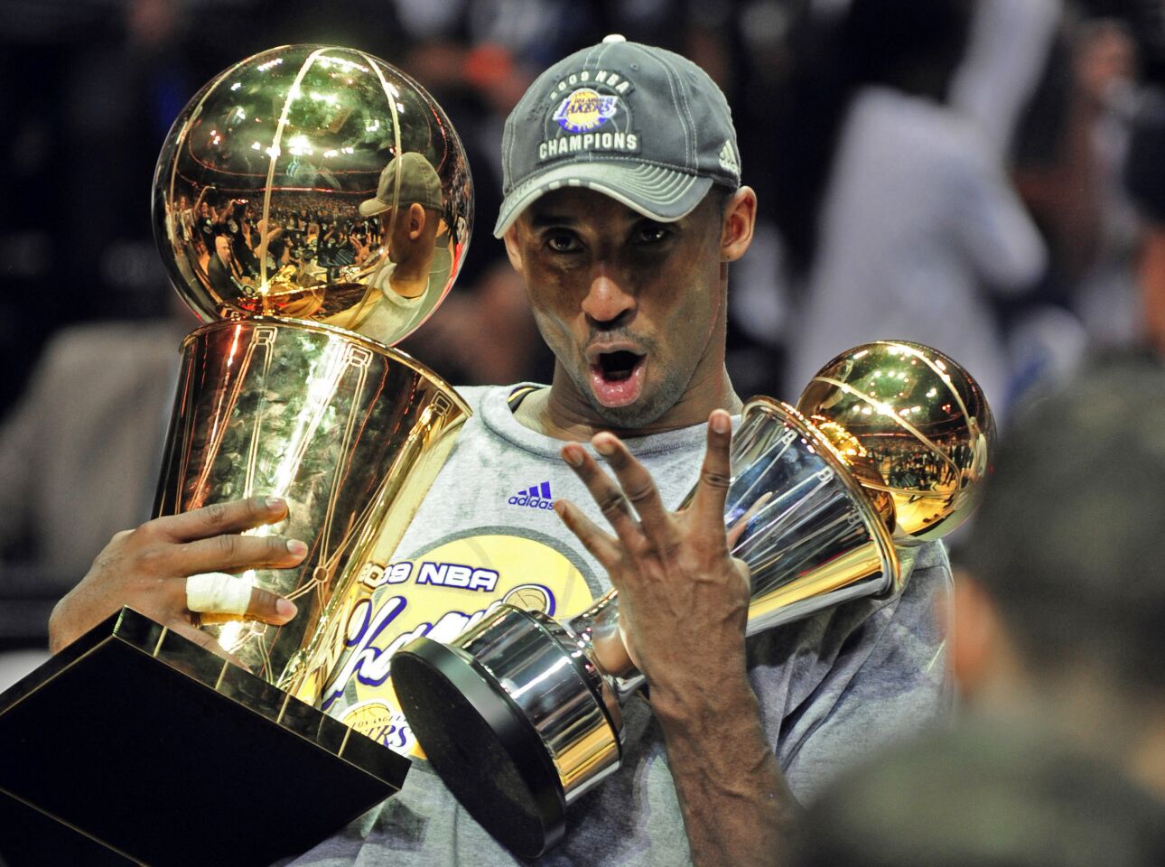 Kobe Bryant holds the championship and Finals MVP trophies and puts up four fingers after winning his fourth title.