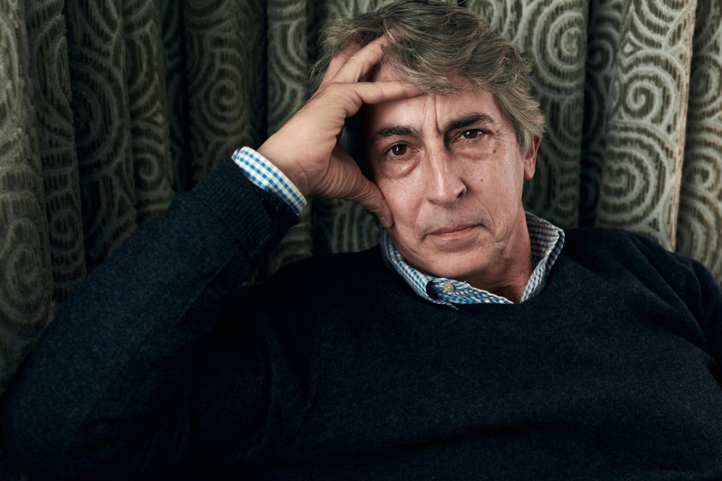 Alexander Payne holds a hand to his head as he poses for a portrait.