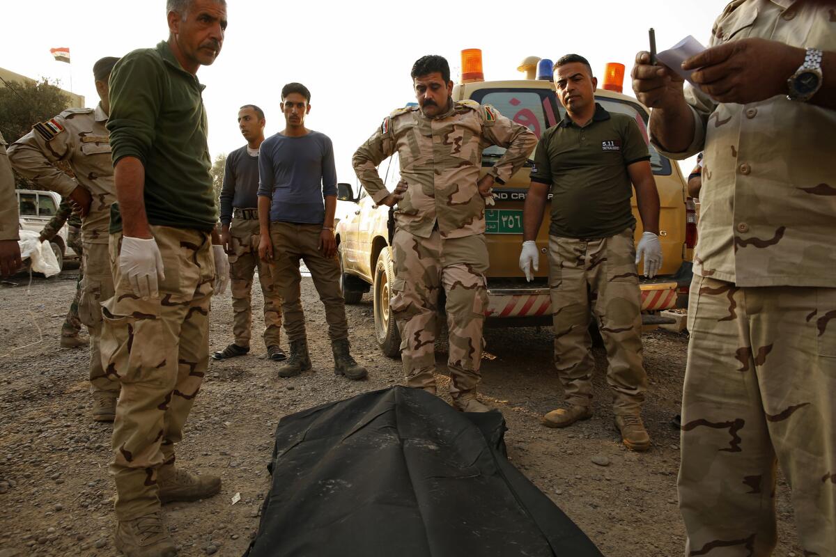 At the Iraqi Army's 9th Armored Division medical clinic, set up in a private home, doctors including Capt. Osama Fuad Rauf, center, gather around the body of a deceased soldier before he is taken to Irbil and on to Baghdad.