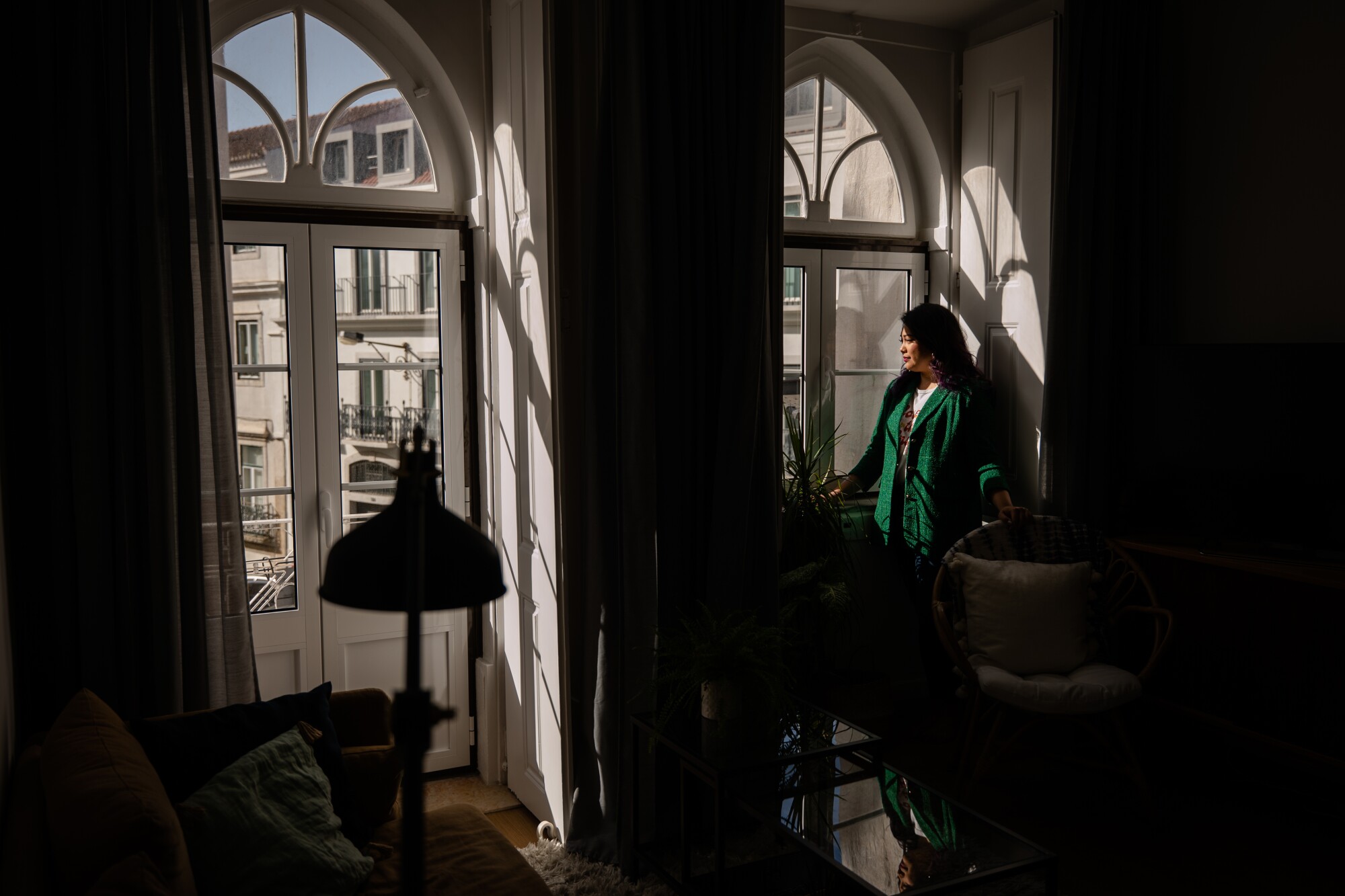 A woman in a green jacket looks out the window at other buildings 