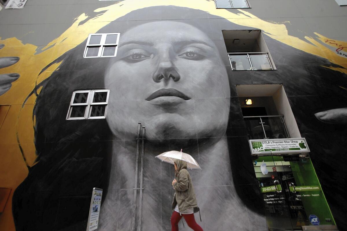 A pedestrian makes her way through the rain past the mural "Our Lady of DTLA" on the SB Tower building on Spring Street.
