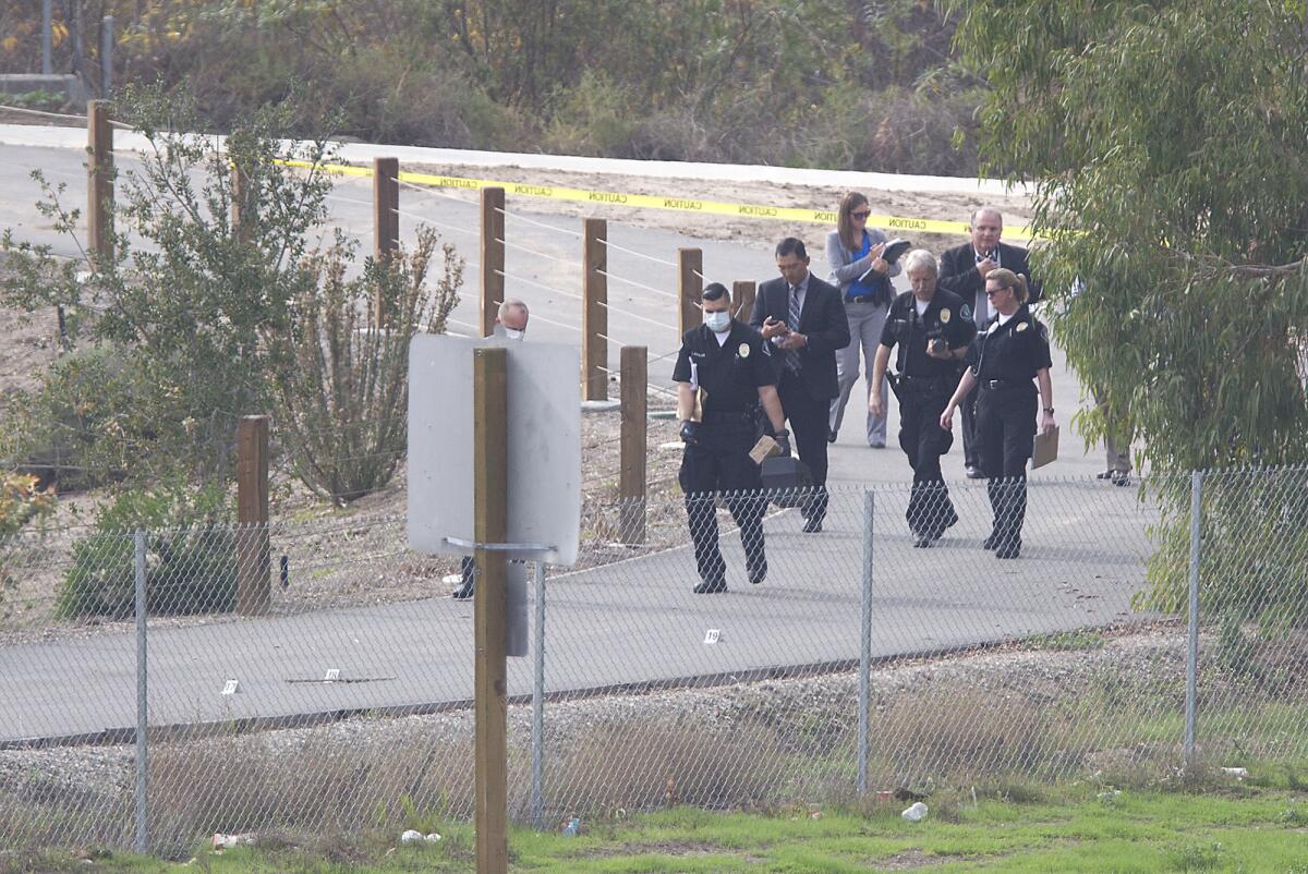 Investigators and others with the Irvine Police Department walk down a bike path next to the 405 Freeway where a body was found on Tuesday in Irvine.