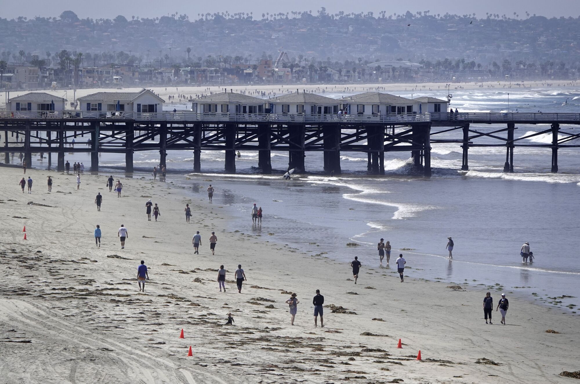 People walk along the coast in Pacific Beach after local beaches reopened to activities such as walking, running, and surfing on April 27, 2020. Beaches have been closed for several weeks due to the coronavirus. The boardwalks and congregating on the sand are still prohibited.