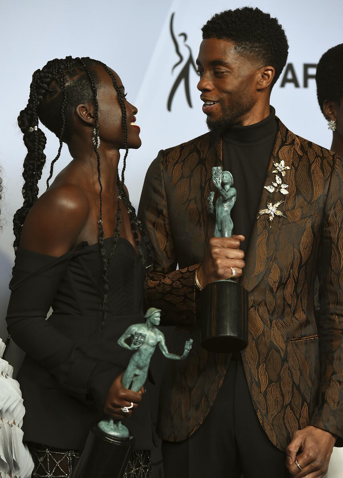 Lupita Nyong'o, left, and Chadwick Boseman look at each other while holding their SAG Awards in 2019