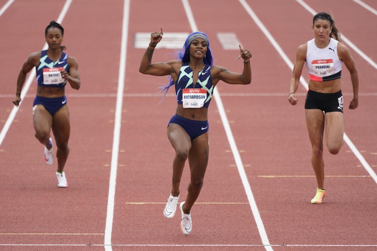 Sha'Carri Richardson gives thumbs up during women's 100-meter dash while two other women run on either side behind her