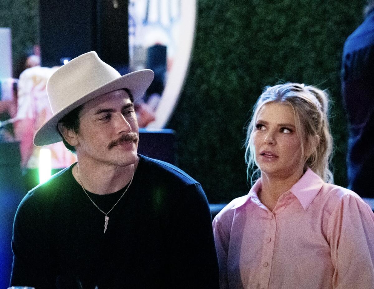 Tom Sandoval in a black shirt and tan hat sits next to Ariana Madix in a pink button-up blouse on 'Vanderpump Rules'
