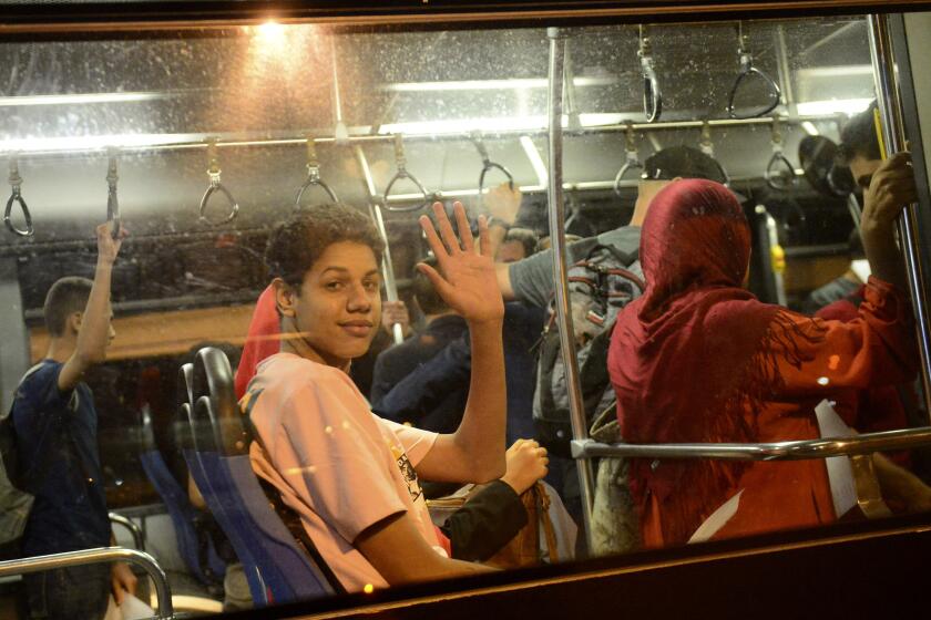 People wave from a bus after arriving in a military plane from Khartoum at the Houari-Boumediene airport in Algiers, Tuesday, April 25, 2023. An Algerian military plane evacuated 94 Algerian citizens but also Palestinians and Syrians people who lived in Sudan. Sudanese and foreigners streamed out of the capital of Khartoum and other battle zones, as fighting Tuesday shook a new three-day truce brokered by the United States and Saudi Arabia. (AP Photo/Amine)