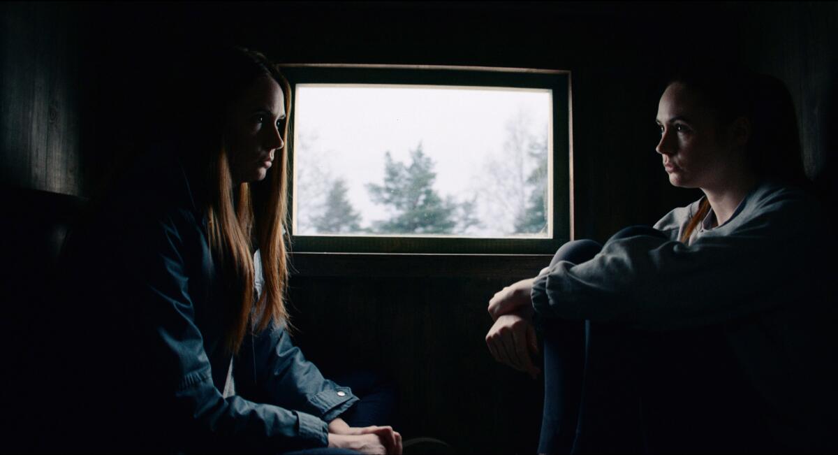 A woman and her clone sit on either side of a window in the movie “Dual.”