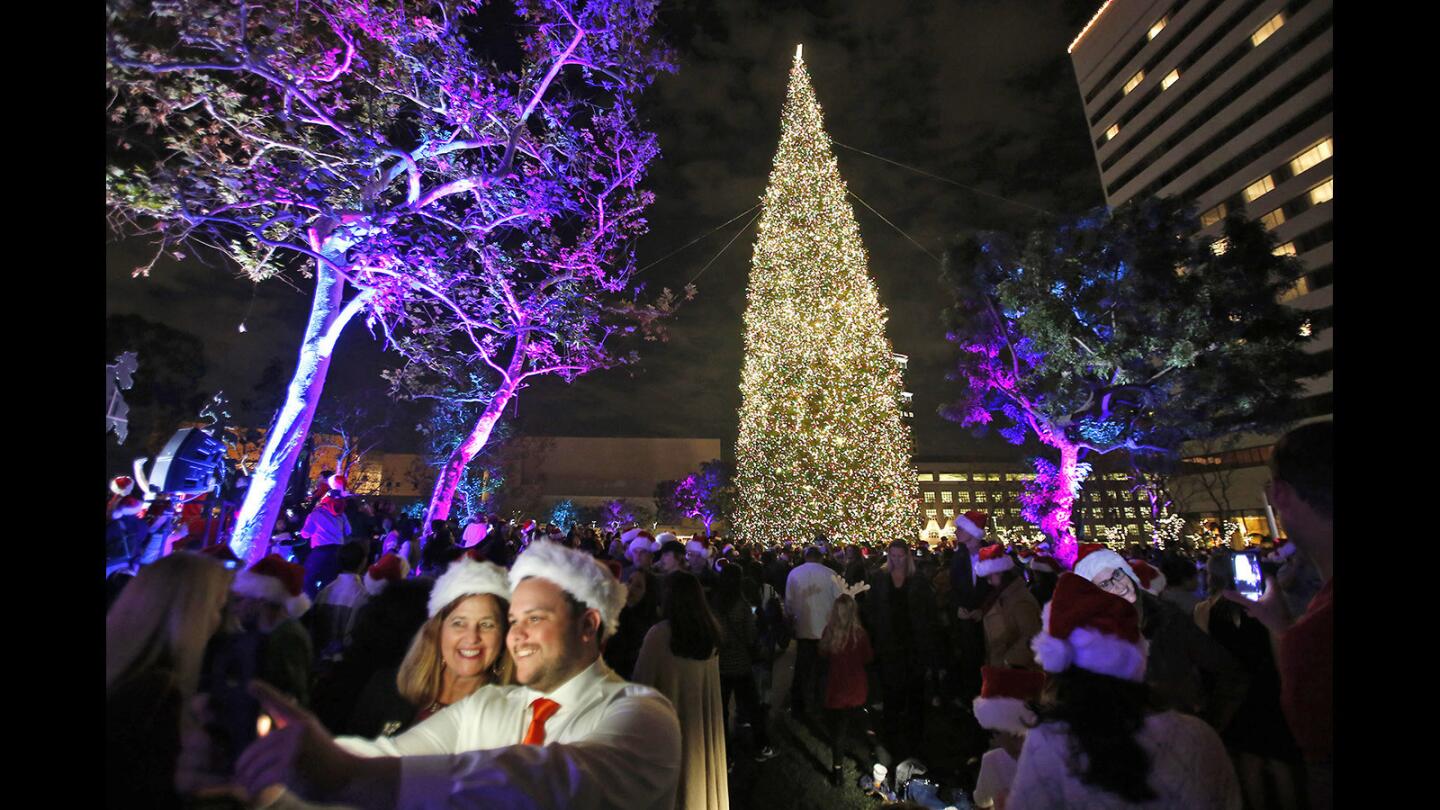 A couple take a selfie in front of the 96-foot white fir during the 36th annual South Coast Plaza tree-lighting ceremony at Town Center Park in Costa Mesa on Thursday night.