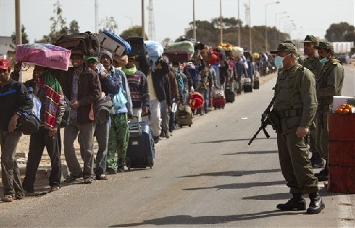 Soldiers from the Tunisia army stand guard as men from Bangladesh, who used to work in Libya but recently fled the unrest, walk with their belongings alongside a road, as they head to a refugee camp after crossing the Tunisia-Libyan border, in Ras Ajdir, Tunisia, Friday, March 4, 2011. Bangladeshis were angry at their country's government for not doing more to get the refugees home. Most of the Bangladeshis appear to have arrived in Tunisia penniless because their Libyan employers did not pay them or because they were robbed on the way. (AP Photo/Emilio Morenatti)