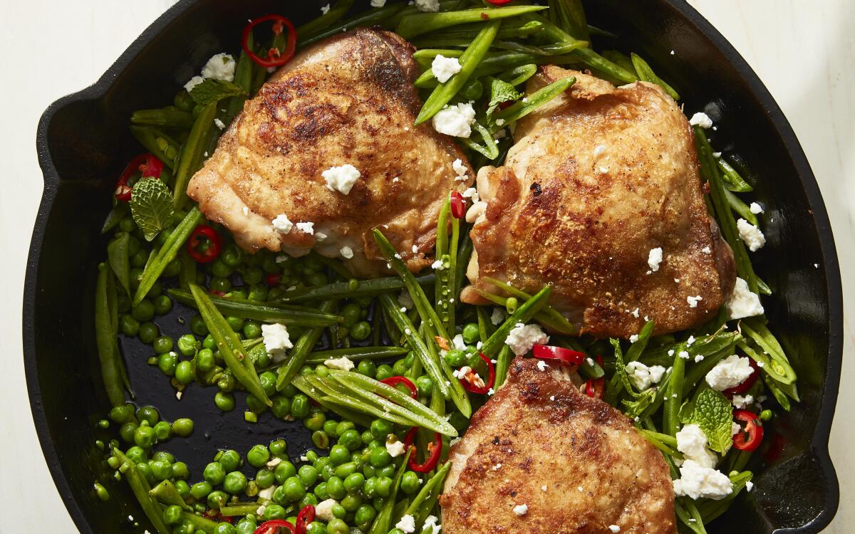 Chicken thighs with peas and red chiles in an iron skillet.