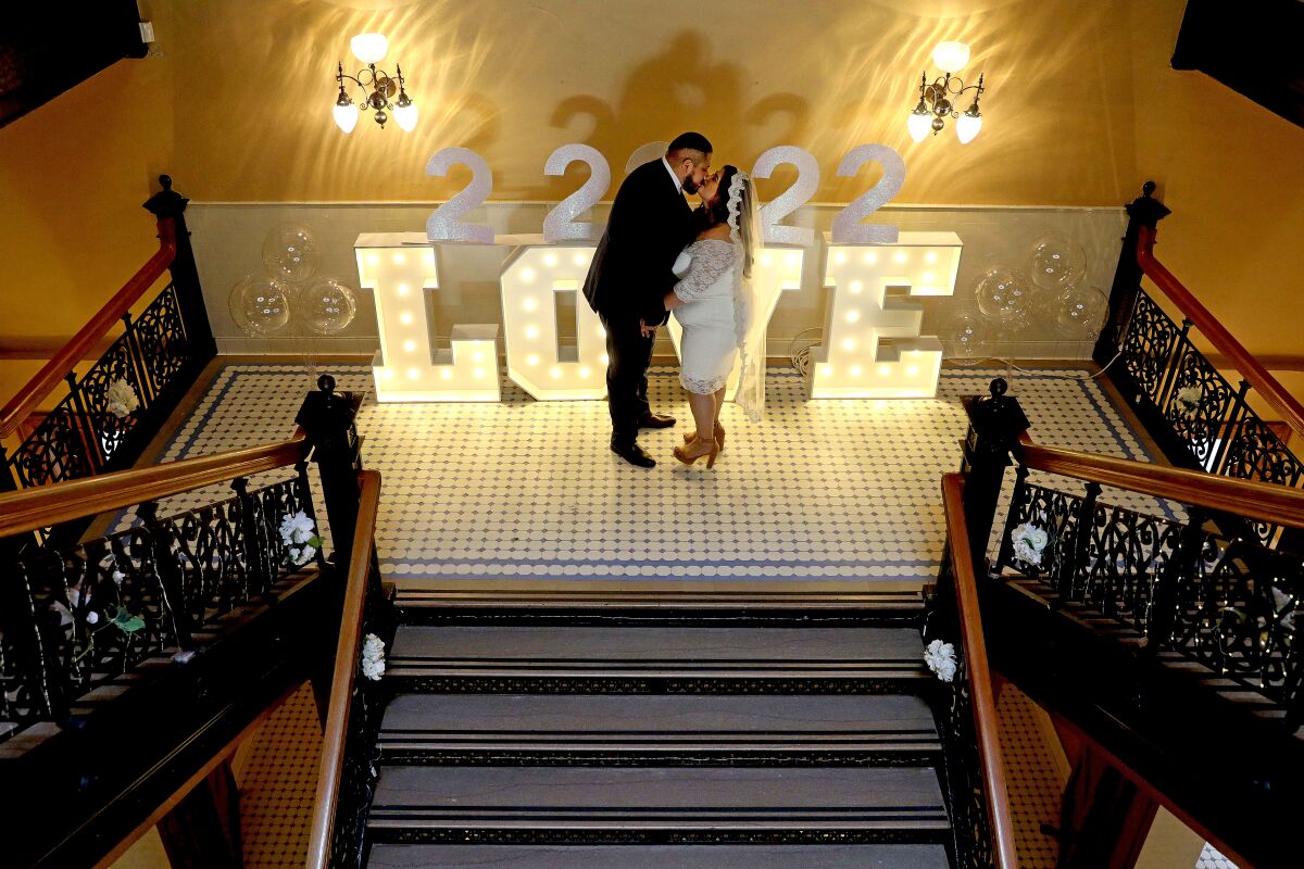 A man and a woman kiss in front of a large sign that reads "2 2 22 love"