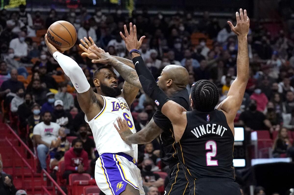 Lakers star LeBron James tries to pass the ball over Miami Heat forward P.J. Tucker and guard Gabe Vincent.