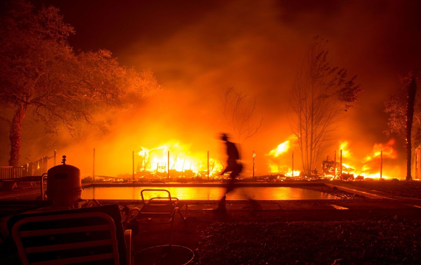 A firefighter walks near a pool as a neighboring home burns in the Napa wine region.