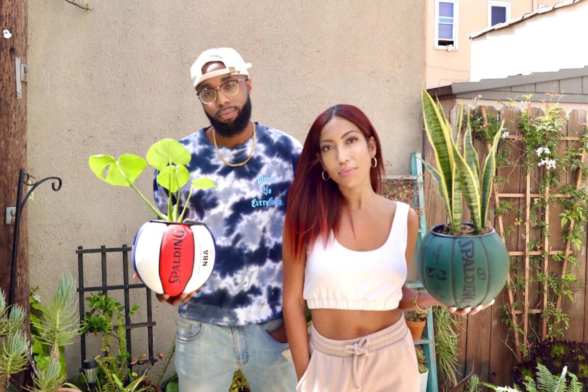 A man and a woman hold basketballs that have been turned into planters.