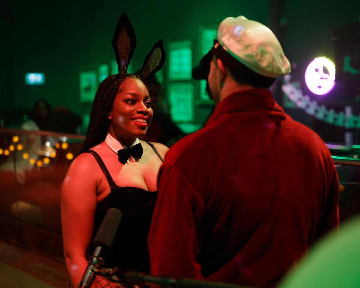 A woman smiling and wearing black bunny ears and a bowtie looking at a man with his back to the camera