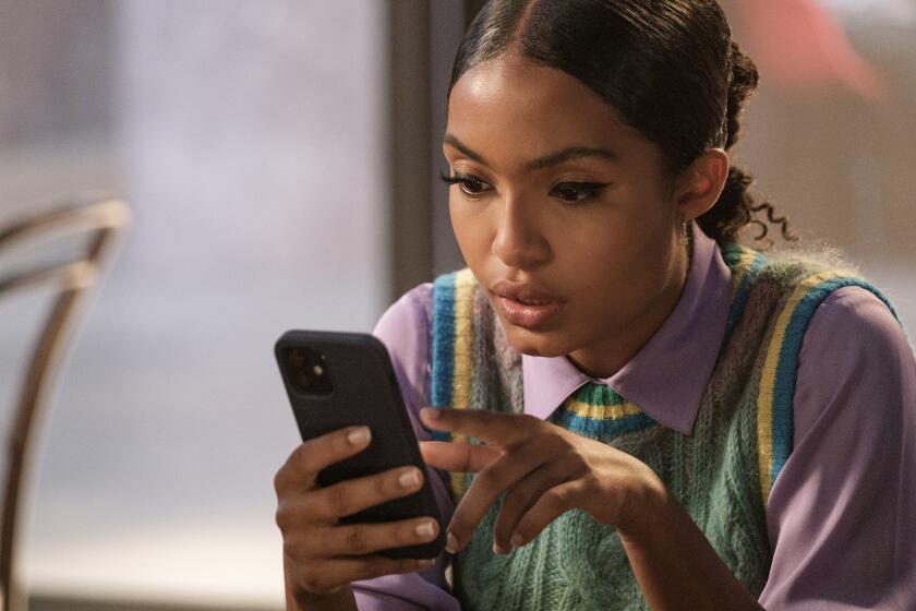 Yara Shahidi wearing a colorful sweater-vest and scrolling through a black smartphone