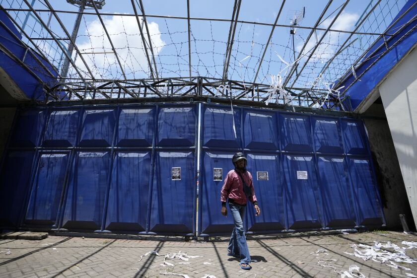 A man walks in front of gate at the Kanjuruhan Stadium in Malang, Indonesia, Tuesday, Oct. 4, 2022. A police chief and nine elite officers were removed from their posts Monday and 18 others were being investigated for responsibility in the firing of tear gas inside a soccer stadium that set off a stampede, killing over 100 people, officials said. (AP Photo/Achmad Ibrahim)