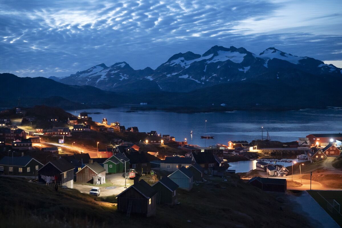 In this photo taken late Friday, Aug. 16, 2019, homes are illuminated after the sunset in Tasiilaq, Greenland. 