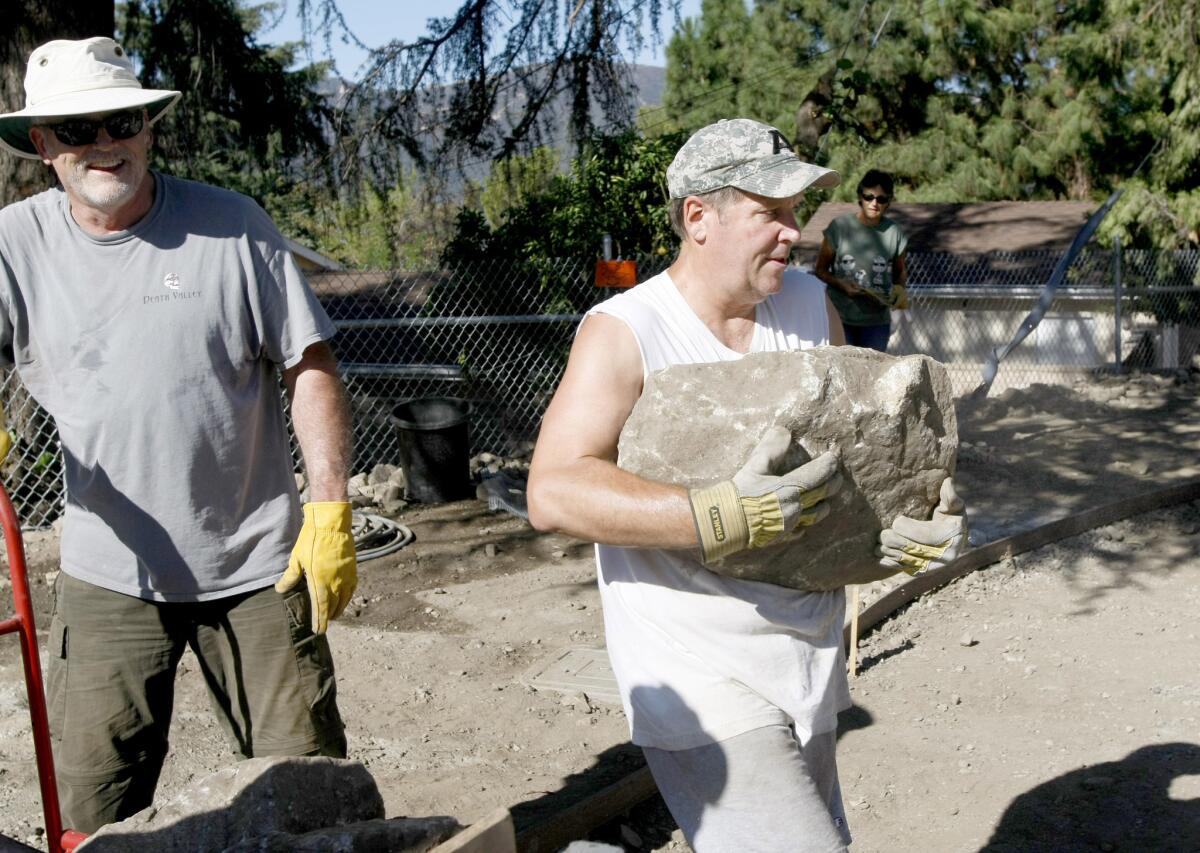 With Mike Claessens left, looking on Frank Paschal, right, carries a large rock at the Crescenta Commons Gathering Spot construction site at Rosemont and Orange in La Crescenta.