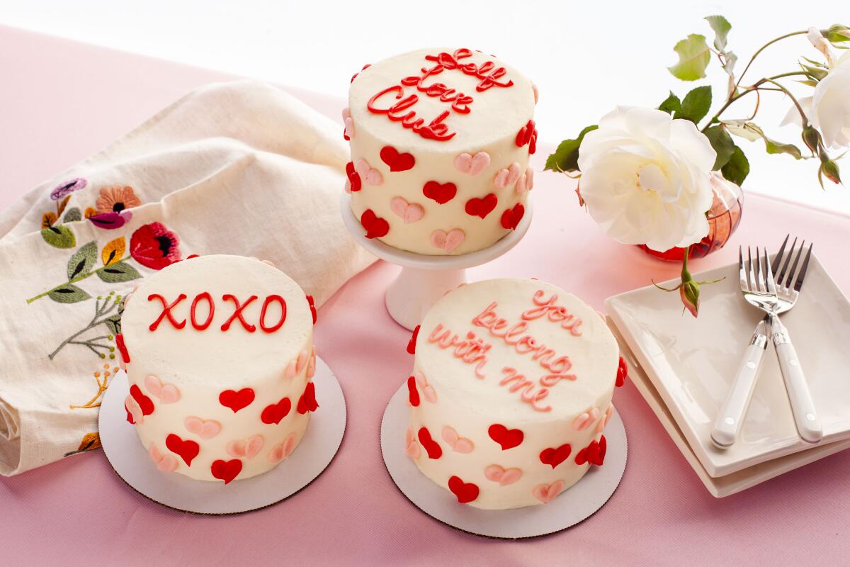 Three white-frosted small cakes decorated with hearts and sweet messages