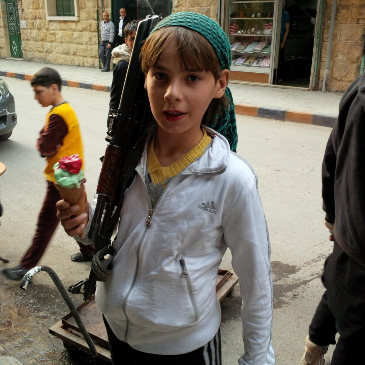 A boy standing with a rifle and an ice cream cone in Aleppo, Syria, says he is a fighter with the Suqoor Al Sham group, a member of the Islamic Front.
