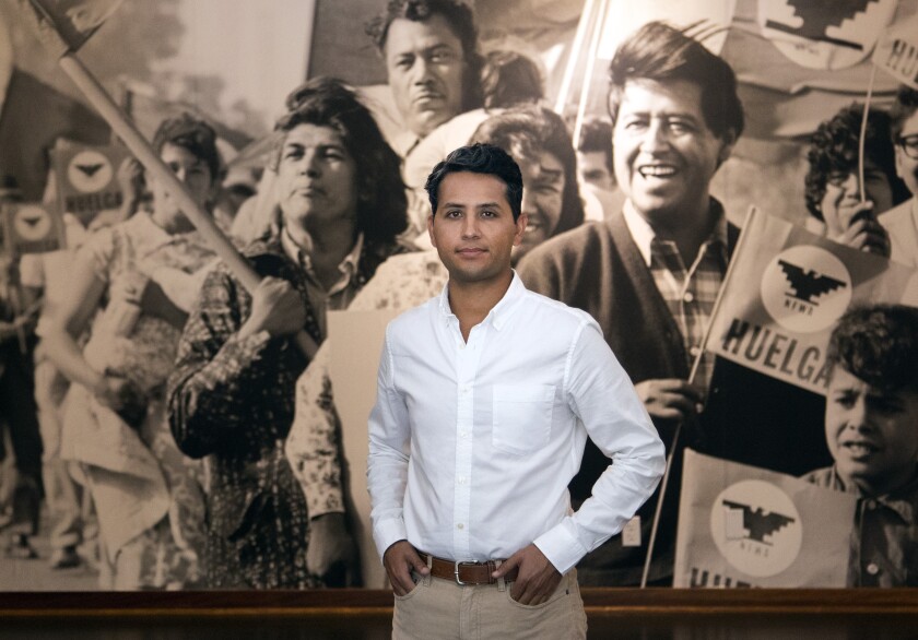 A man in a white shirt stands before an old photograph.