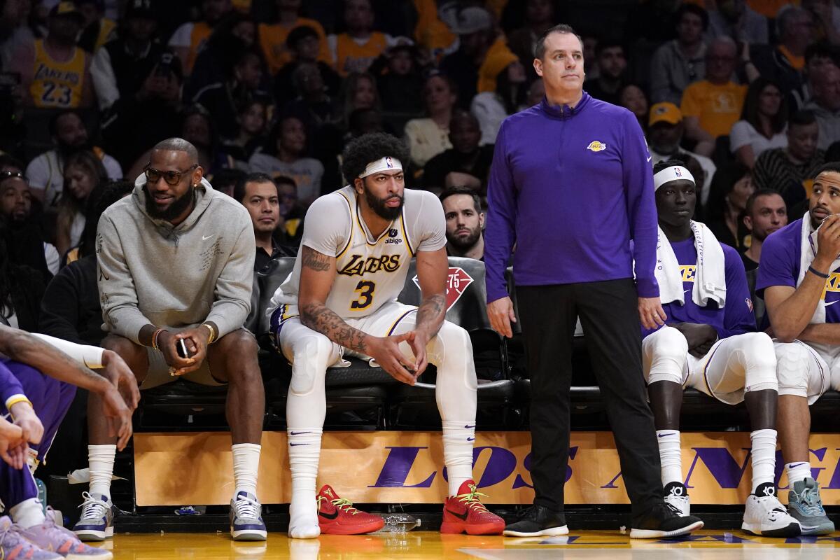 Lakers forward LeBron James sits on the bench next to forward Anthony Davis as head coach Frank Vogel stands.