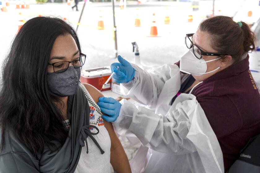 RIVERSIDE, CA - FEBRUARY 1, 2021: Middle school teacher Michelle Survillas, left, of Riverside gets the Moderna vaccine from vaccinating nurse Natalie Murone in the parking lot of the Riverside Convention Center on February 1, 2021 in Riverside, California. Currently, this site is capable of giving 500 vaccinations a day in one of the regions hardest hit by the pandemic. Only residents 65 and older and educators are eligible for the vaccination here.(Gina Ferazzi / Los Angeles Times)